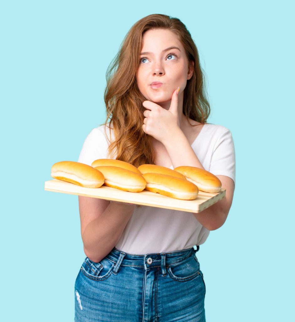 Nő gondolkozik, kezében tálcán hotdog-kiflik